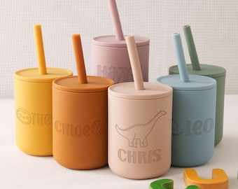 May include: A collection of six cylindrical silicone cups with matching lids and straws in various muted colours. Each cup features a debossed name and a simple line-art graphic, including a sloth, strawberry, dinosaur, and watermelon design.