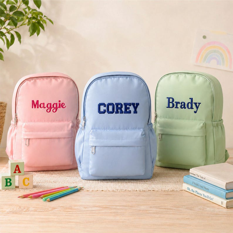 three personalized backpacks with the names " Maggie", " Corey", and " Brady" printed on them, along with a few books and a plant.