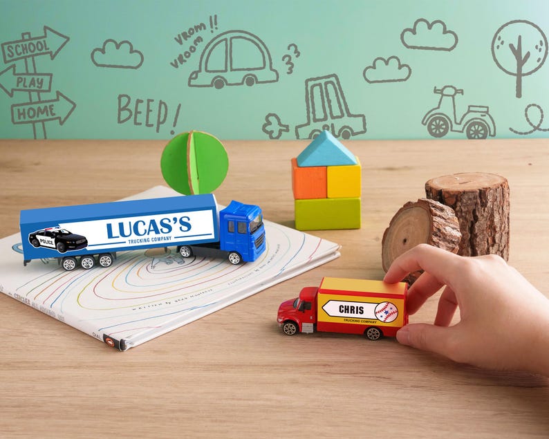 A child's hand is reaching for a toy truck on a wooden surface, with a toy train and other toys nearby. The background features a wall with various drawings and text, including words like "BEEP!" and "VROOM!" and other playful elements.