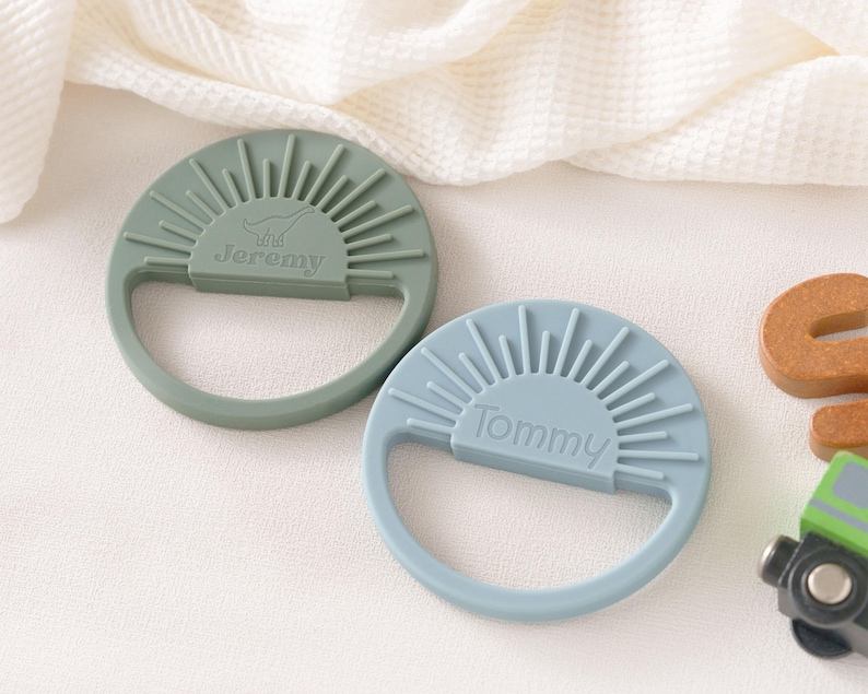 two baby teething toys with personalized names on them, placed on a white surface.