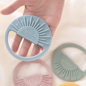 A hand holding a teething ring with the name 'Adam' written on it.