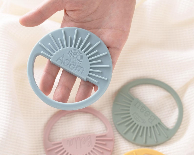 A hand holding a teething ring with the name 'Adam' written on it.