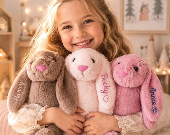 May include: Three plush stuffed bunnies with long ears and pink noses. The brown bunny has the name Harry embroidered on its ear. The light pink bunny features the name Becky and a heart. The dark pink bunny displays the name Annie and a flower.