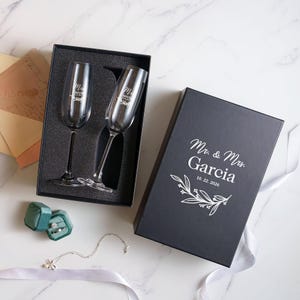 a set of two champagne glasses, a wedding ring box, and some other wedding-related items arranged on a marble surface.