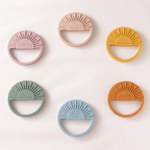 six colorful teething rings, each with a unique design and color, arranged in a circular pattern on a white background.