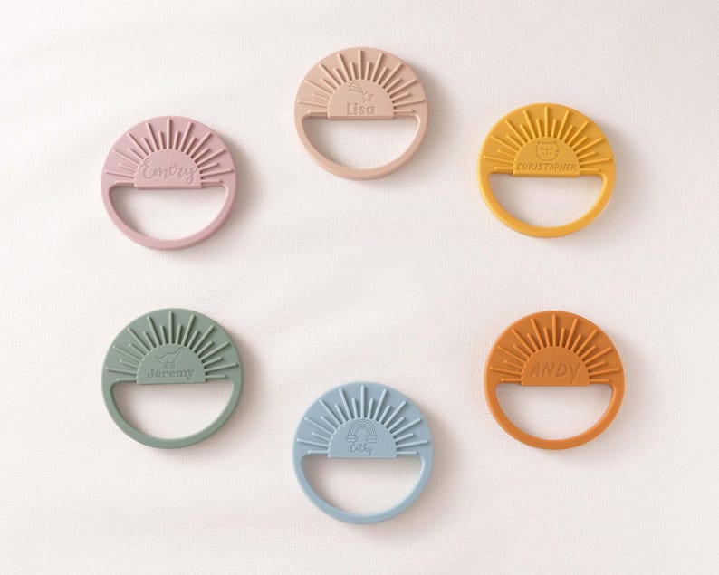 six colorful teething rings, each with a unique design and color, arranged in a circular pattern on a white background.