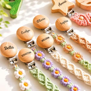 May include: A collection of pacifier clips featuring round or star-shaped wooden discs engraved with the names Bella, Sebastian, Evelyn, William, Olivia, Sophia, and Anna, attached to macrame cords with crocheted flower patterns in pastel colors.