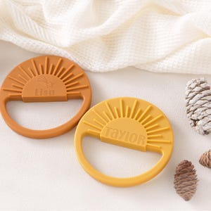 two orange and two yellow sun-shaped baby teething toys, along with some pine cones, arranged on a white surface.