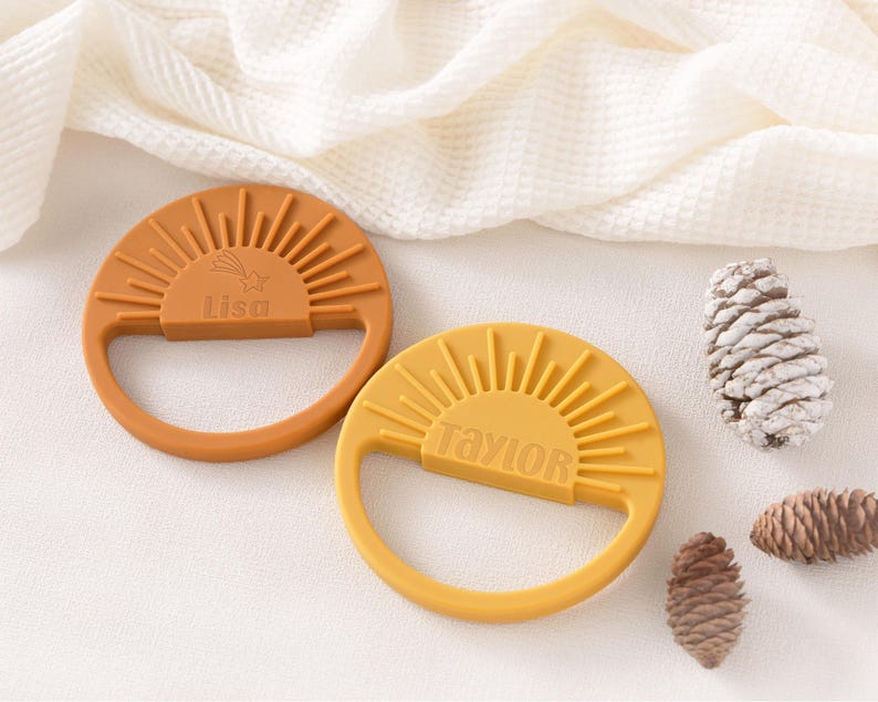 two orange and two yellow sun-shaped baby teething toys, along with some pine cones, arranged on a white surface.