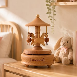 A wooden carousel music box with a wooden horse and a wooden ball is placed on a wooden dresser next to a stuffed rabbit.