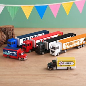 A collection of toy trucks and a toy car on a wooden surface, with colorful flags hanging in the background.