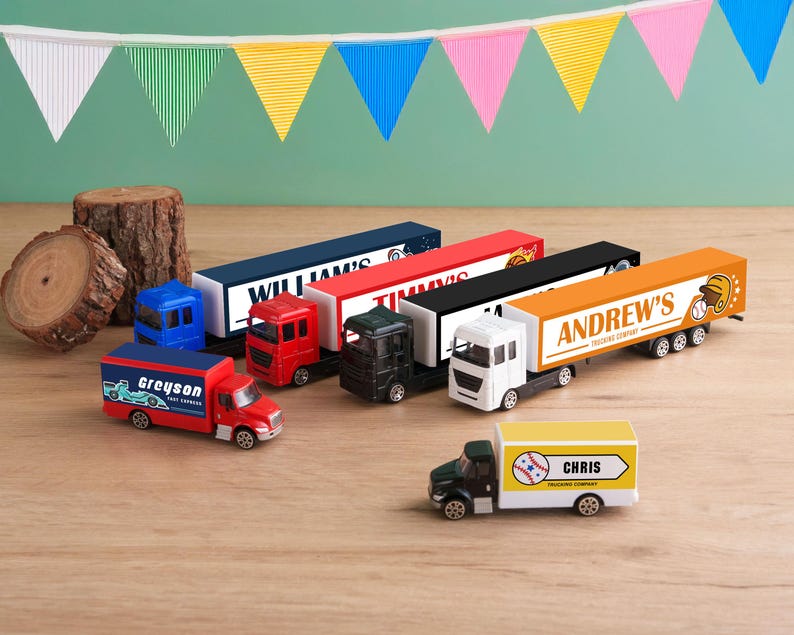 A collection of toy trucks and a toy car on a wooden surface, with colorful flags hanging in the background.