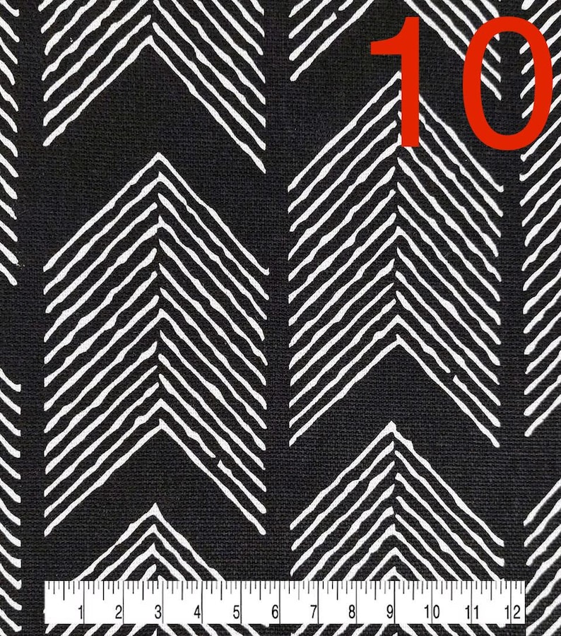 May include: Black fabric with a white chevron pattern. The fabric is measured with a ruler in inches. The number 10 is written in red on the fabric.