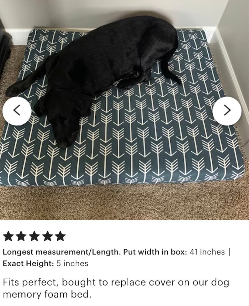 May include: A dark gray dog bed with a white arrow pattern. The bed is 41 inches wide and 5 inches high. A black dog is lying on the bed.