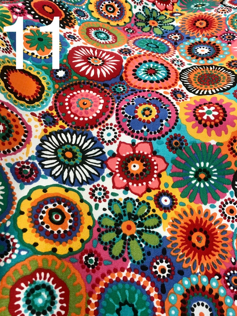 May include: Colorful fabric with a repeating pattern of circles and flowers. The circles are filled with dots and the flowers have a central circle with petals around it. The fabric is white with a variety of colors including red, orange, yellow, green, blue, and purple.