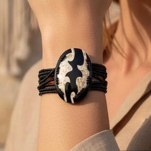 May include: Black and white oval bracelet with a unique design. The bracelet features a black band with multiple strands and a central oval stone with a contrasting white pattern. A stylish accessory.