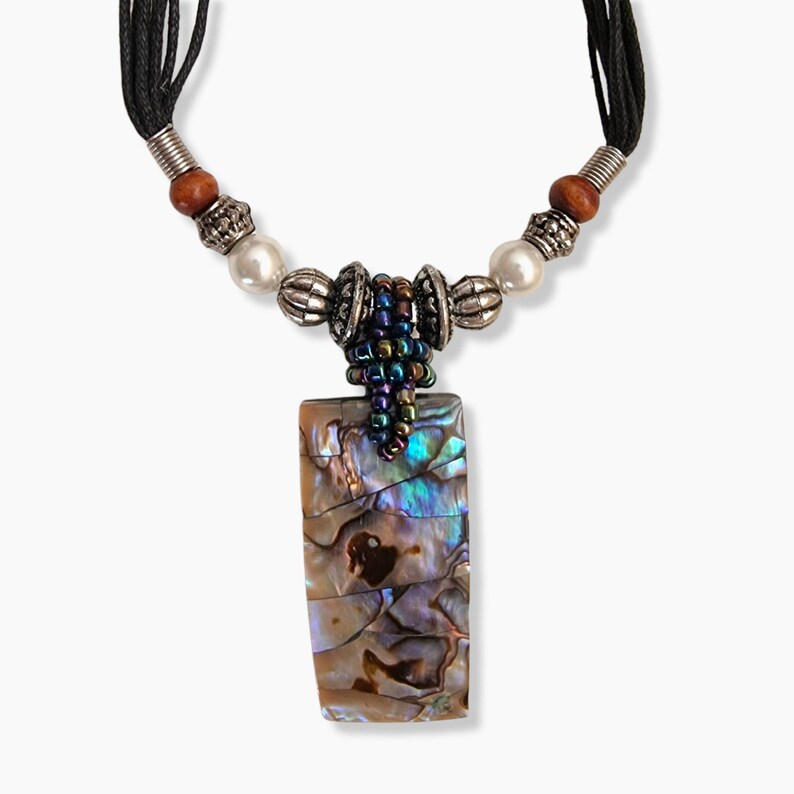 May include: A rectangular pendant necklace with a mother-of-pearl design. The pendant is attached to a black cord necklace with silver-colored beads, wooden beads, and faux pearls. The pendant has iridescent colors of blue, green, and brown.