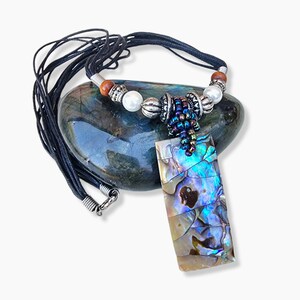May include: Abalone shell pendant necklace with a rectangular shape. The pendant has iridescent blue, green, and gold hues. The necklace features a black cord, silver beads, and a beaded cluster.