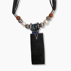 May include: A black pendant necklace with a rectangular shape. The necklace features a black cord, silver-colored beads, pearls, and a cluster of iridescent beads. The pendant is a solid, dark color.