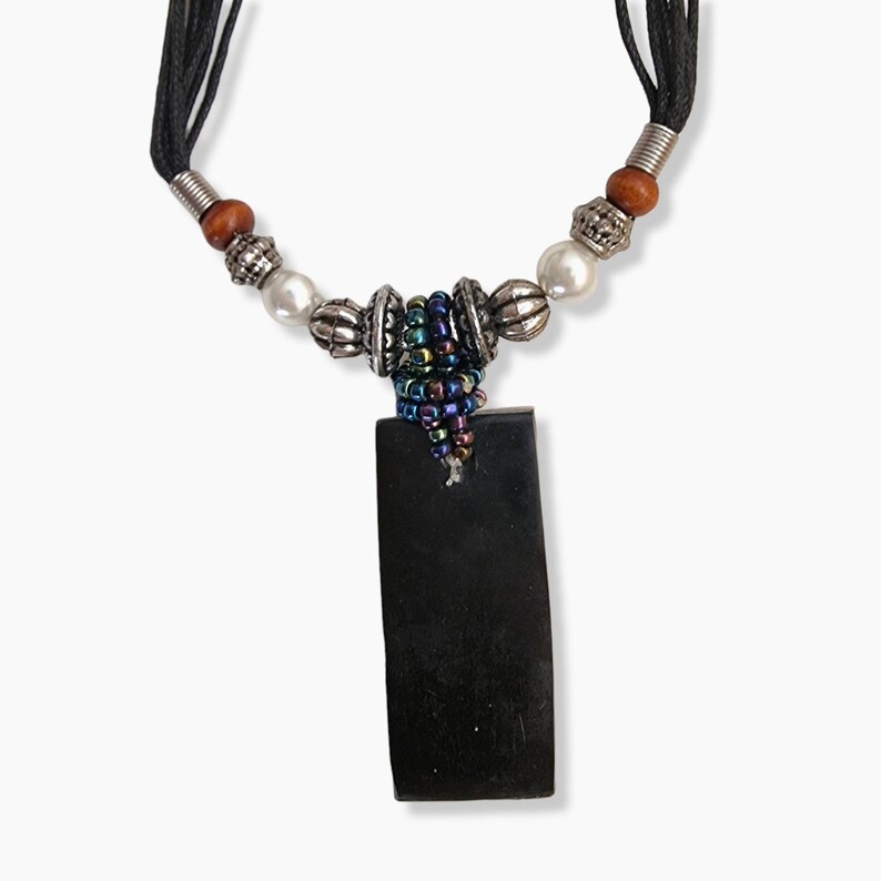 May include: A black pendant necklace with a rectangular shape. The necklace features a black cord, silver-colored beads, pearls, and a cluster of iridescent beads. The pendant is a solid, dark color.