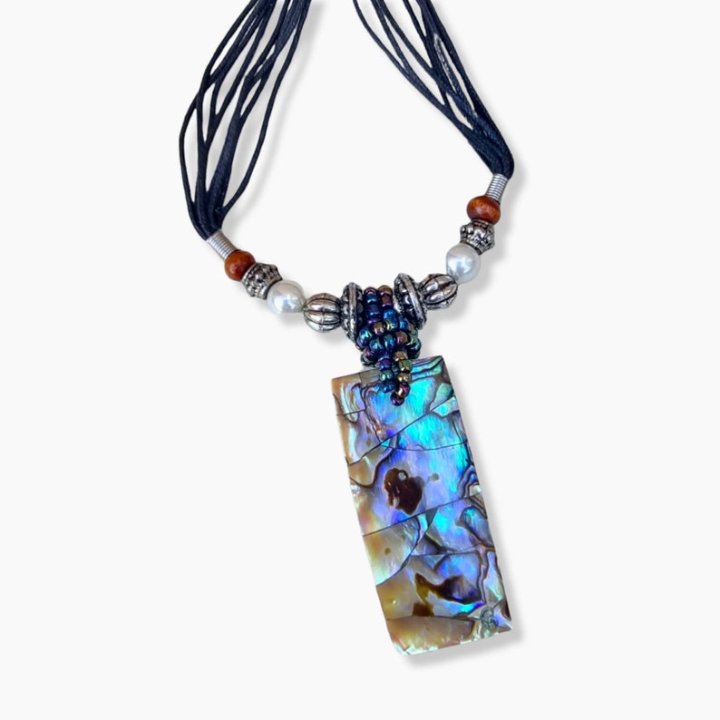 May include: A rectangular pendant necklace with a black cord. The pendant is a rectangle with iridescent blue, green, and brown colors. The necklace has silver beads, pearls, and wooden beads.
