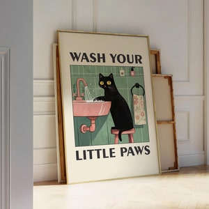 Peut inclure: Un chat noir aux yeux jaunes se lave les pattes dans un lavabo rose. Le texte "WASH YOUR LITTLE PAWS" est imprimé sur l'affiche.