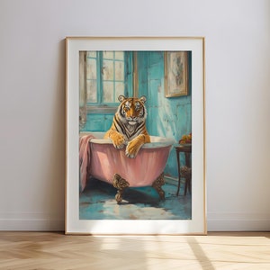 May include: Framed art print featuring a tiger relaxing in a pink claw-foot bathtub. The tiger has orange and black stripes. The bathroom has blue walls and a window. A pink towel is draped over the tub's edge. The artwork is in a gold frame.