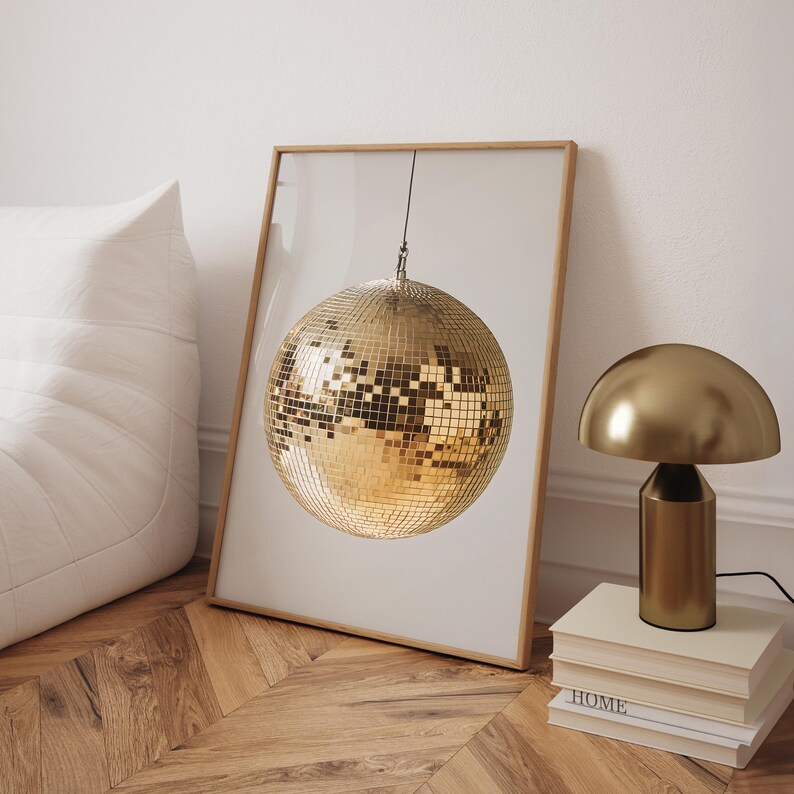 May include: A gold disco ball hanging from the ceiling in a framed print. The print is on a white background and is sitting on a wooden floor.