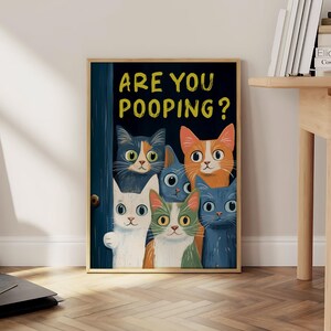 May include: A framed poster with a blue background and the text "ARE YOU POOPING?" in yellow. Five cartoon cats with different colored fur are peeking out from behind a blue door.