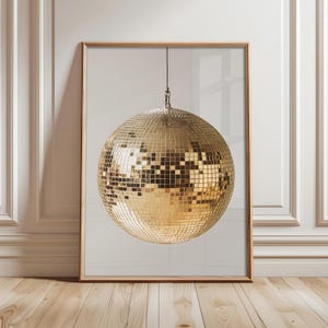 May include: A gold disco ball hanging from the ceiling against a white background. The disco ball is made of many small mirrored squares.