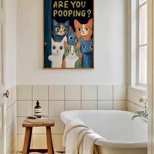 May include: A framed print with a humorous illustration of a group of cats peeking through a door with the text "Are you pooping?" The cats are various colors, including orange, white, and blue. The print is hanging on a white tiled wall in a bathroom.
