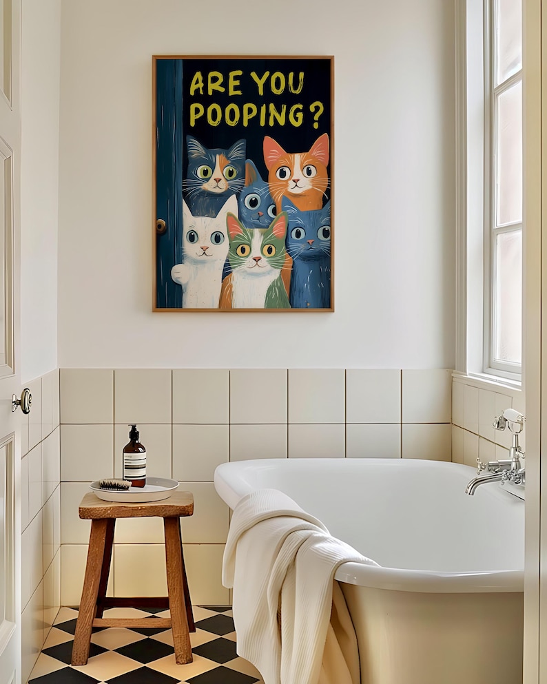 May include: A framed print with a humorous illustration of a group of cats peeking through a door with the text "Are you pooping?" The cats are various colors, including orange, white, and blue. The print is hanging on a white tiled wall in a bathroom.