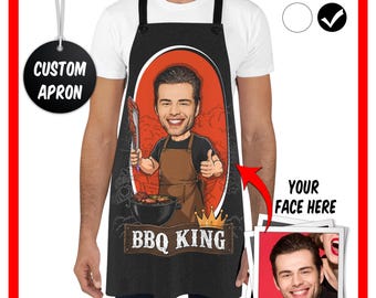 May include: A black apron featuring a cartoon illustration of a person wearing a brown apron, holding tongs, and giving a thumbs up. The design includes a red oval background, a gold crown, and the text BBQ KING. A photo insert shows a face.
