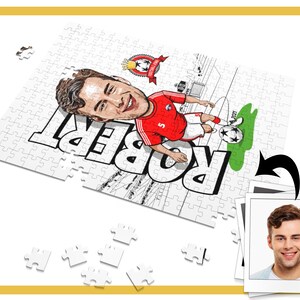 May include: A white jigsaw puzzle with a cartoon illustration of a soccer player in a red and white jersey. The puzzle is partially assembled and the player's name "Robert" is visible. A photo of a man is in the background.