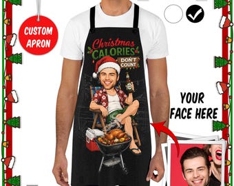May include: A black apron featuring a graphic of a person in a Santa hat sitting in a chair, holding a beer, with a grill and turkey below. The text reads Christmas CALORIES DON'T COUNT. The design includes a customizable face area.