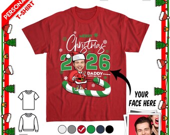 May include: A red short-sleeved t-shirt featuring a graphic of a cartoon character wearing a Santa hat with a personalized face, the text Merry Christmas 2026, and the word DADDY. The design includes a green and white candy cane element.