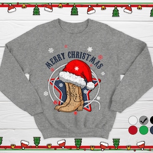 Puede incluir: Una sudadera gris con un diseño navideño. El gráfico presenta una bota de vaquero, un gorro de Papá Noel y las palabras "MERRY CHRISTMAS" en un círculo. Copos de nieve y una estrella completan el tema festivo.