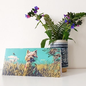 May include: A greeting card featuring a cartoon illustration of a white dog with brown ears in a field of green grass. The dog is looking to the right. The background is a light blue sky with white clouds. The card is blank inside.
