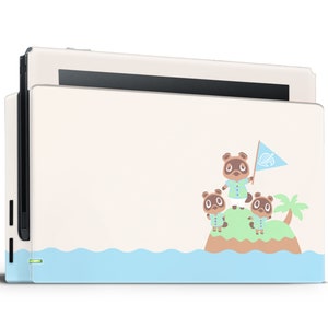 May include: A white Nintendo Switch console with a custom skin featuring Tom Nook and two villagers from the Animal Crossing video game series. The skin has a light blue ocean wave design at the bottom and a green island with palm trees in the center. Tom Nook is holding a flag with the Animal Crossing logo.