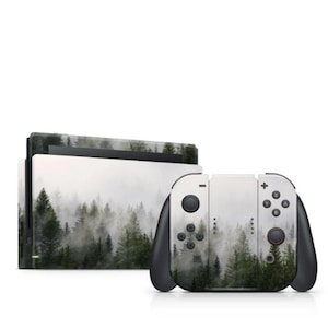Peut inclure: Une console de jeu blanche et noire et des manettes avec un motif de forêt. Le motif représente une forêt brumeuse avec de grands arbres verts. Les manettes ont des poignées et des boutons noirs. La console est blanche avec un dessus noir.