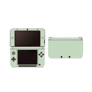 May include: A light green Nintendo 3DS XL console with a top and bottom screen. The console has a black trim and buttons. The console is shown next to a matching light green Nintendo 3DS XL bottom cover.