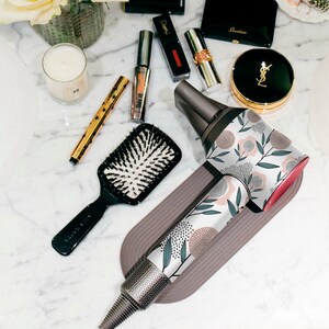 May include: A white and pink floral patterned hair dryer with a gray and white handle. The hair dryer is on a gray and white stand.