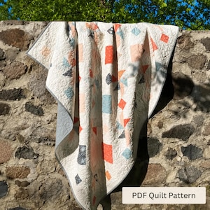 May include: A quilt featuring a white background with an intricate swirling quilted texture and a geometric pattern of scattered squares and triangles in shades of coral, light blue, and dark gray. The text PDF Quilt Pattern is visible.