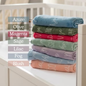 May include: A stack of seven folded blankets in various colors, including azure, olive, magenta, sage, lilac, fog, and blush. Each blanket has white text. The blankets are stacked on a white surface, with a white crib in the background.
