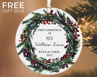 May include: White ceramic Christmas ornament with a green wreath, red berries, and pine cones. The ornament reads "First Christmas at 453 Willow Lane Kyle & Carol 2022".