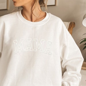 May include: White sweatshirt with the word "MAMA" in a white outlined, collegiate-style font.