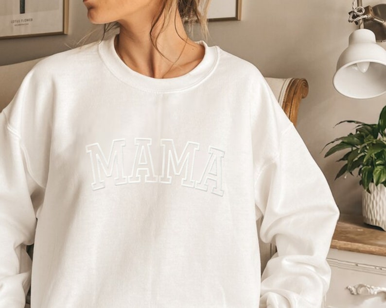 May include: White sweatshirt with the word "MAMA" in a white outlined, collegiate-style font.