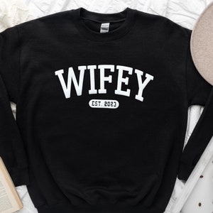 May include: Black sweatshirt with white text that reads "WIFEY EST. 2023" in an arched font.