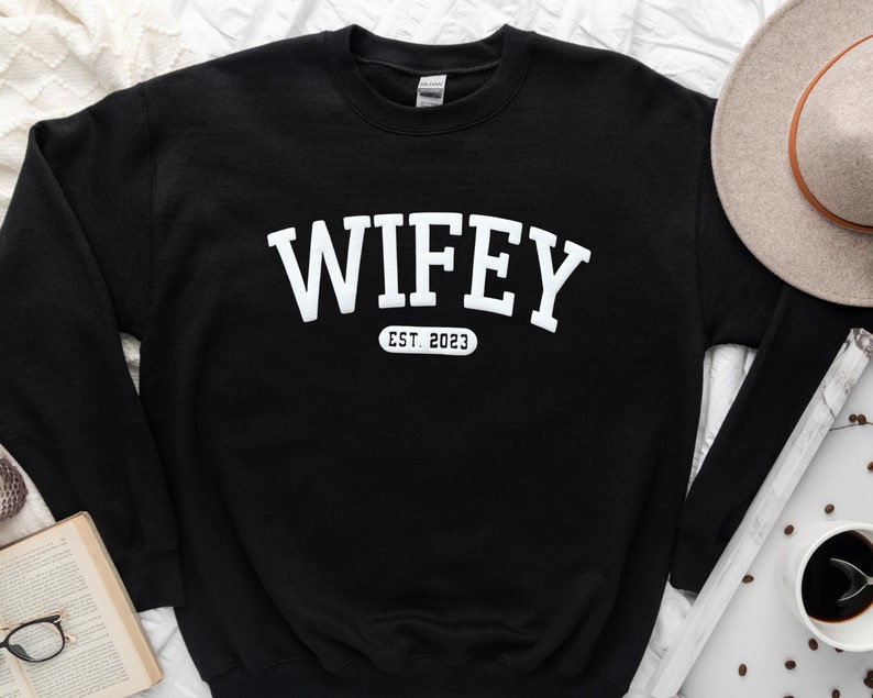 May include: Black sweatshirt with white text that reads "WIFEY EST. 2023" in an arched font.