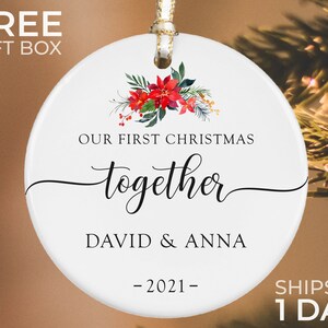 Puede incluir: Adorno navide&ntilde;o de cer&aacute;mica blanca con dise&ntilde;o floral y el texto "OUR FIRST CHRISTMAS together DAVID & ANNA -2021-". El adorno tiene una cinta dorada para colgar, una decoraci&oacute;n festiva.